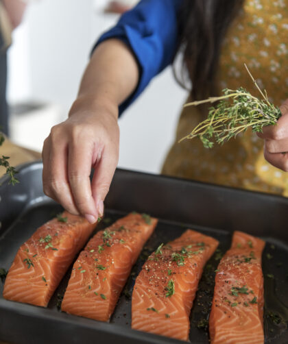 Woman adding spices and herb to raw salmon